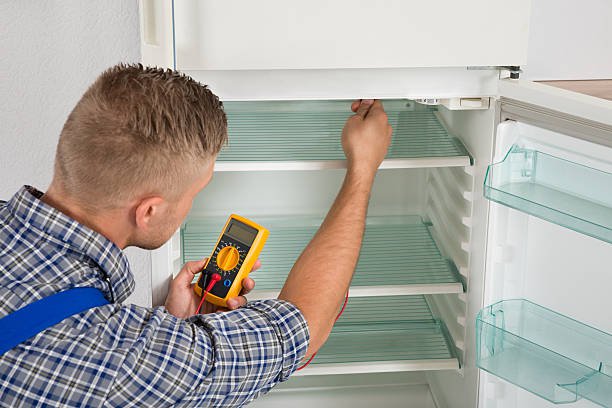Young Male Technician Checking Fridge With Digital Multimeter